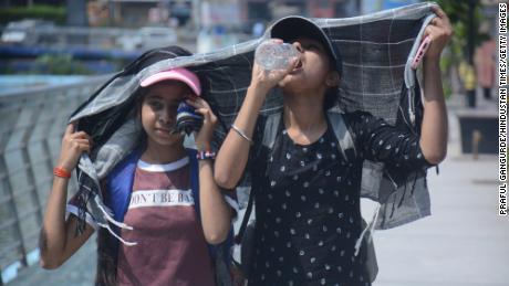 Girls cover their heads as they walk and drink water in the scorching afternoon heat of Mumbai.