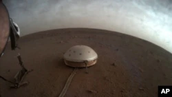 На этом недатированном изображении, предоставленном НАСА в четверг, 22 июля 2021 года, облака плывут над закрытым куполом сейсмометром SEIS посадочного модуля InSight на Марсе.