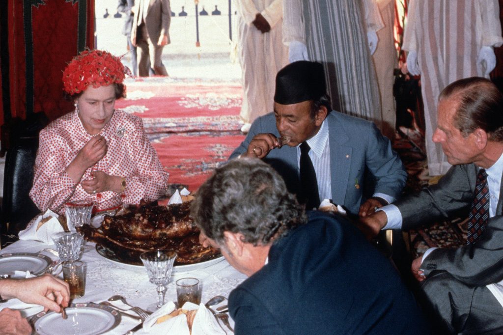 Queen Elizabeth II, Prince Philip, Duke of Edinburgh and King Hassan eat with their hands while attending a feast in the desert on October 27, 1980 in Morocco.