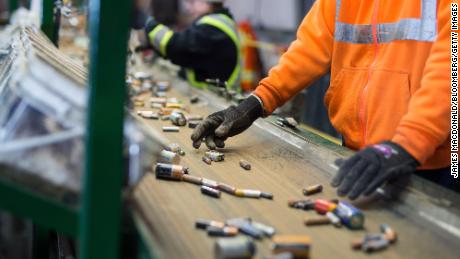 Employees sort batteries that move along a conveyor belt at a recycling facility.