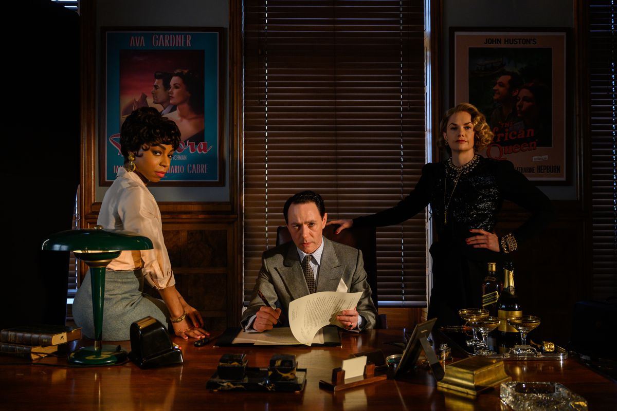 John Wolfe (Rice Shersmith), Petola Spencer (Rita Wilson) and Anne Savile (Peppa Bennett Warner) look out from behind Wolfe's large, shiny desk.